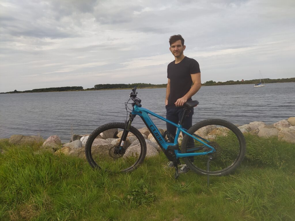 Tamas standing besides his bike in front of the sea