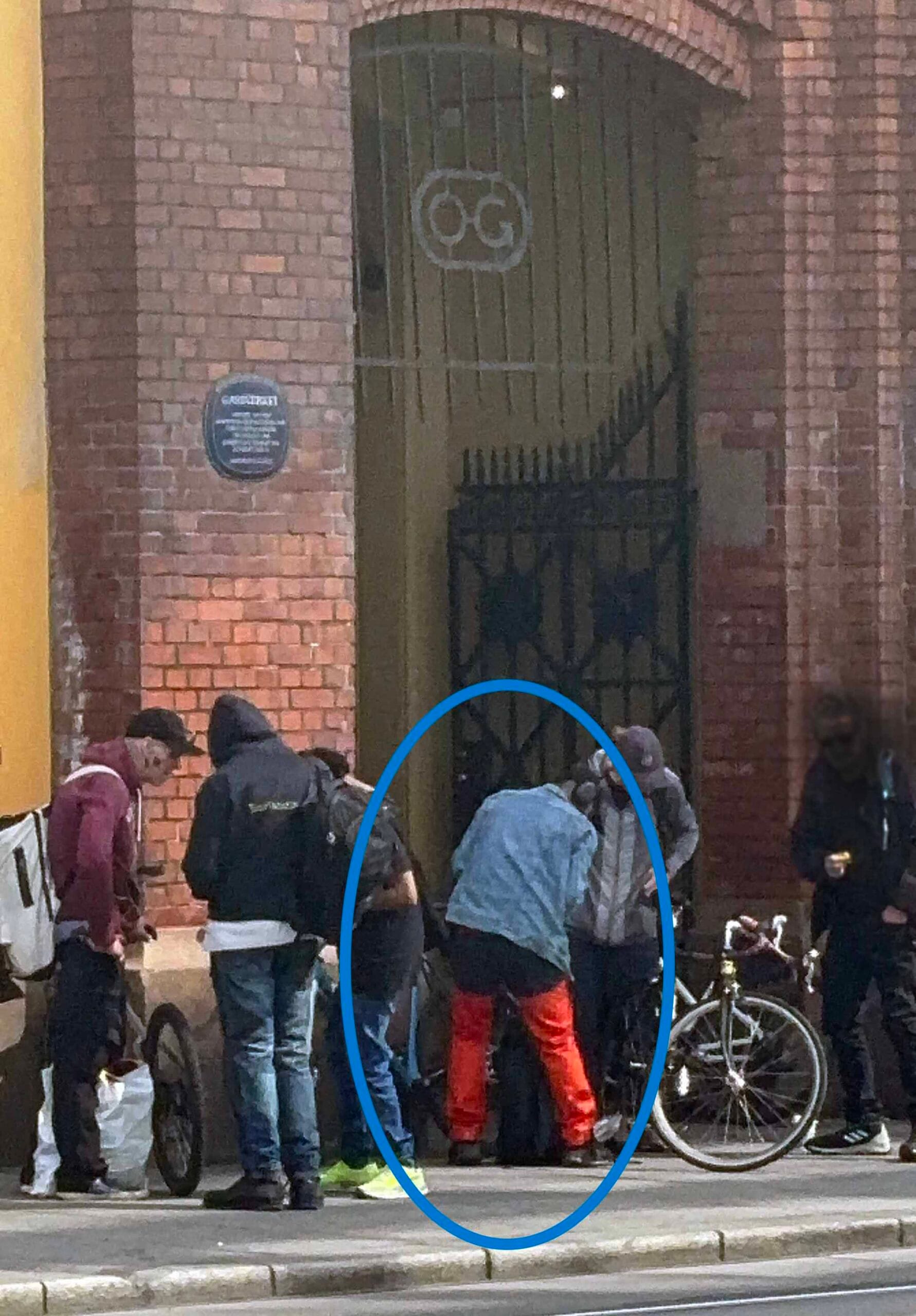 Bike theft in Oslo: man in red pants seen with stolen bicycle surrounded by group on sidewalk near brick archway, Oslo S, Bjørvika 