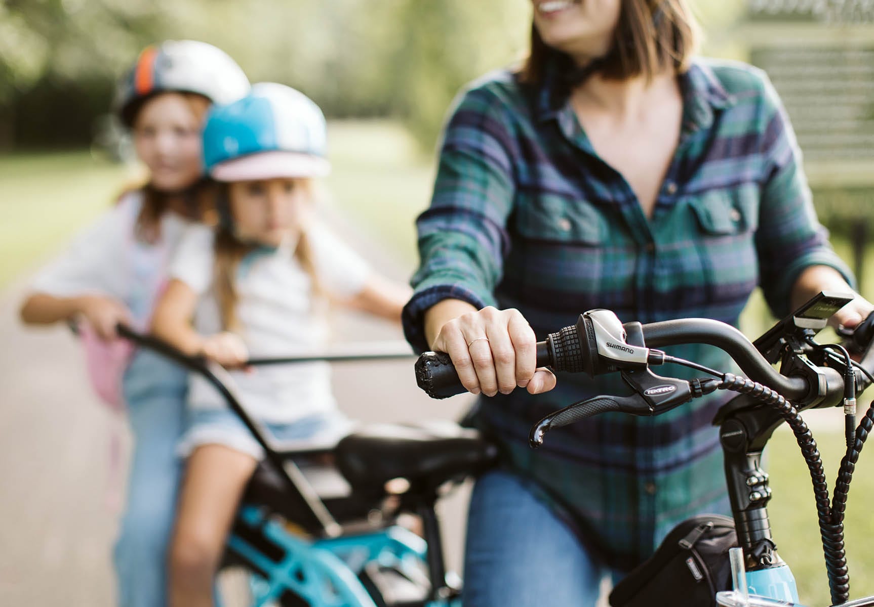 Close-up of a mom’s hand on the handlebar of a blue cargo bike with a hidden BikeFinder tracker, carrying two kids wearing helmets on the back during a school run.