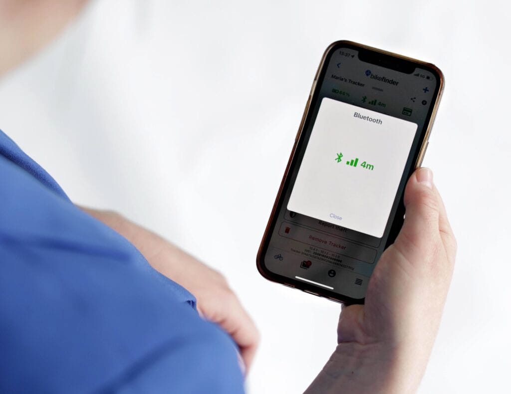 A cyclist uses the BikeFinder app showing a 4m Bluetooth signal from the Advanced Tracker for precise bike location and theft recovery.